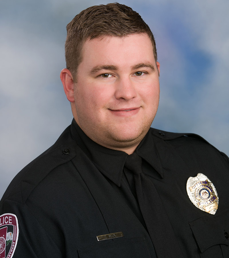 Portrait of Officer Lucas Aycox with short brown hair wearing a black police uniform with a silver badge. 