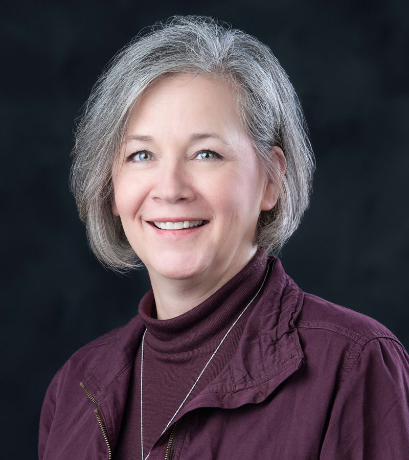 Portrait of Marsha Curry with short grey hair wearing a maroon shirt and jacket. 