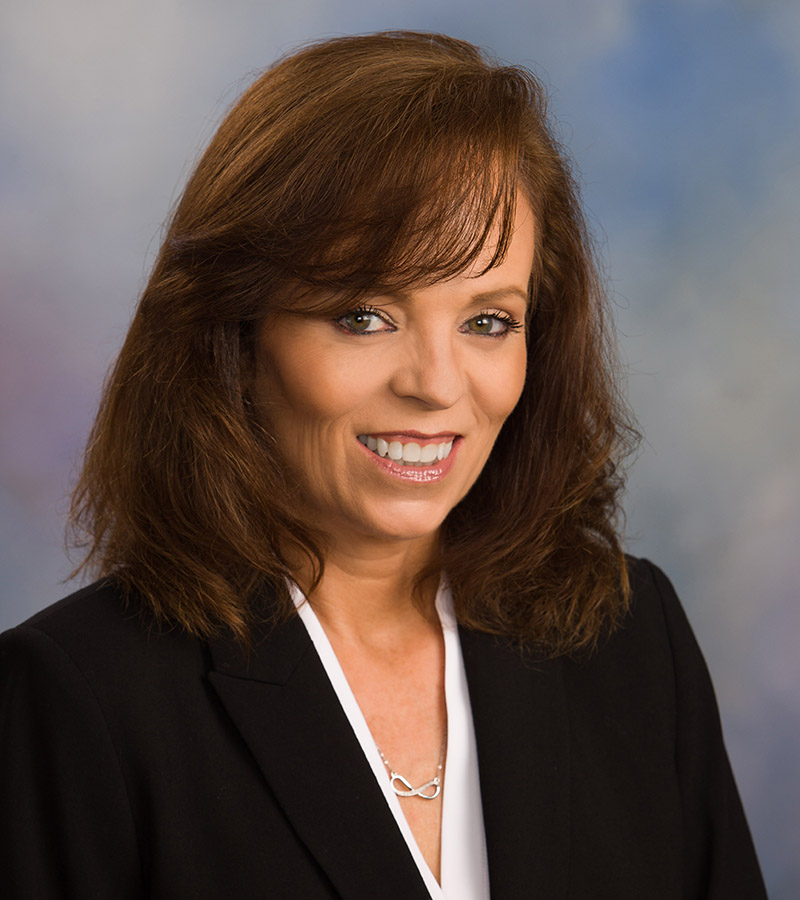 Portrait of Jennifer Haught with shoulder length brown hair and bangs wearing a black blazer with a white shirt