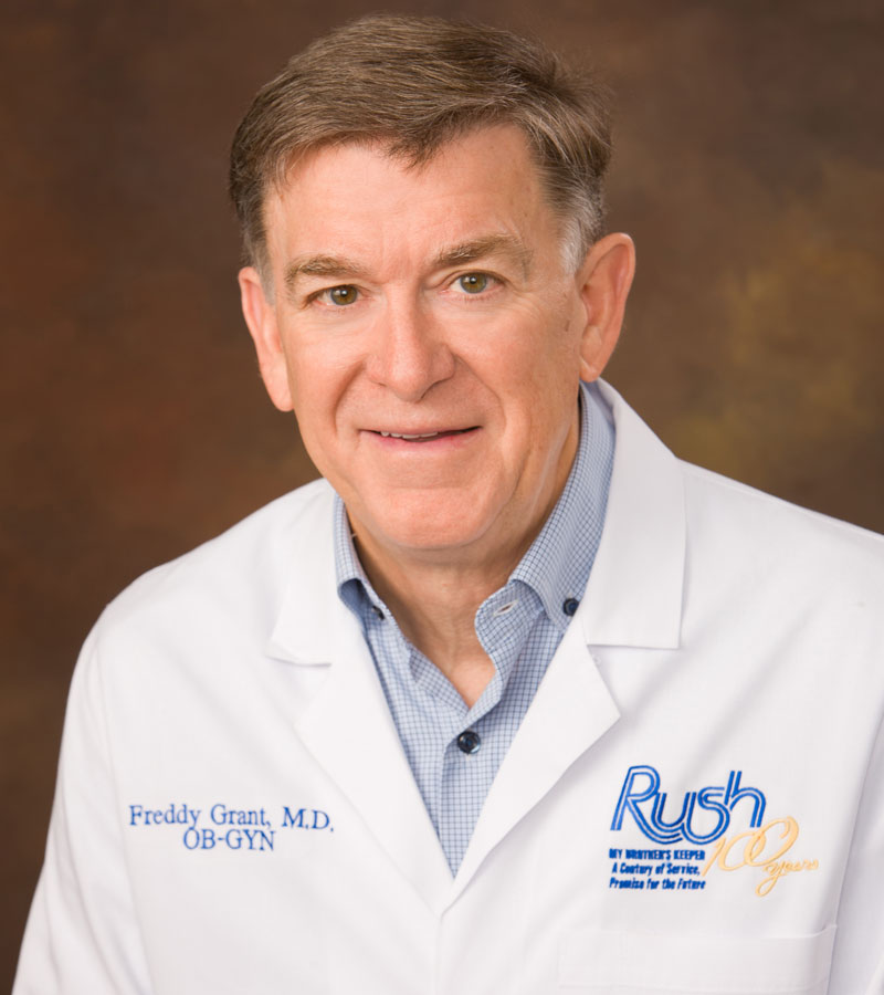 Portrait of Dr. Freddy Grant wearing a white lab coat with the Rush Foundation Hospital logo and a blue shirt.