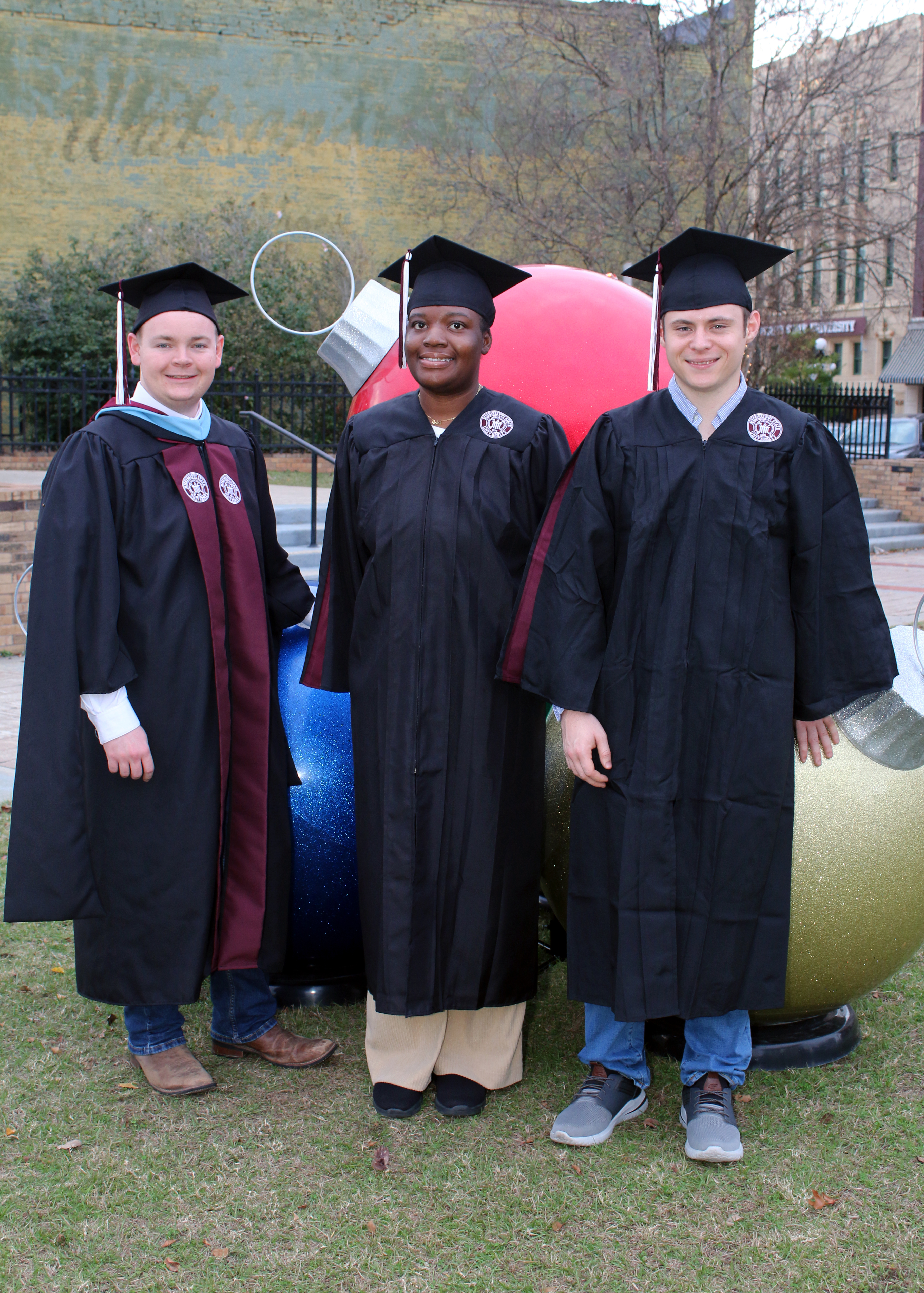 three individuals in graduation cap and gown 