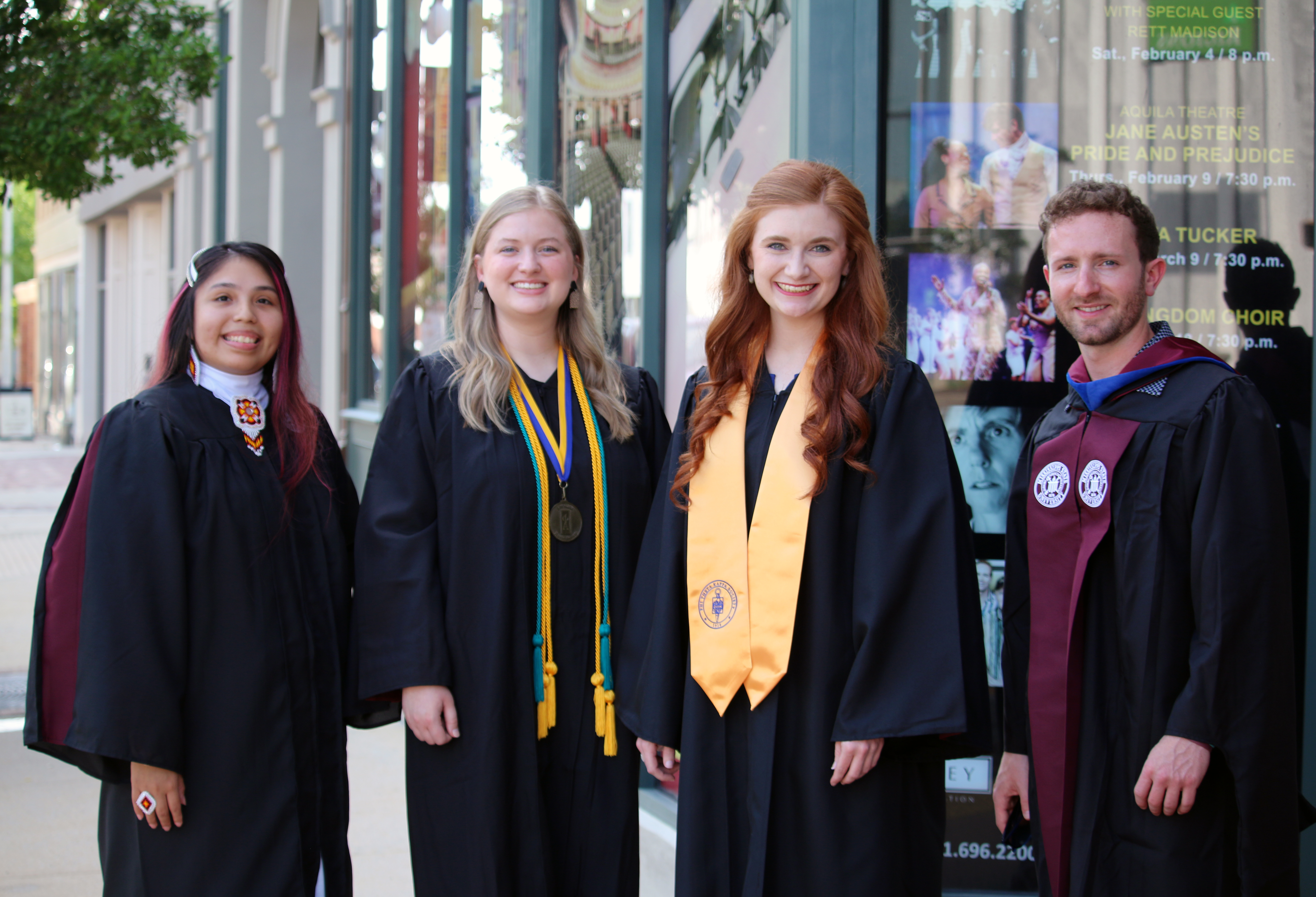 Four students 3 females and 1 male in commencement regalia