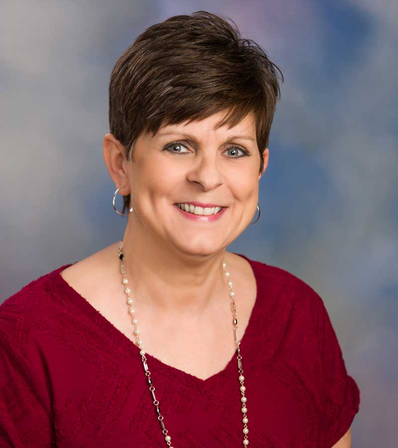 Portrait of Mindy Huebner with short brown hair, wearing a red shirt with a long necklace.