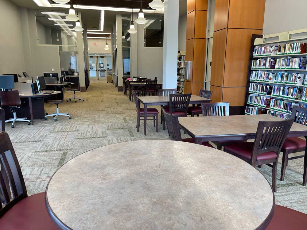 View of the library from the corner of the book section looking out toward the books and study area with computer options toward the front desk and computer lab through to the sitting area
