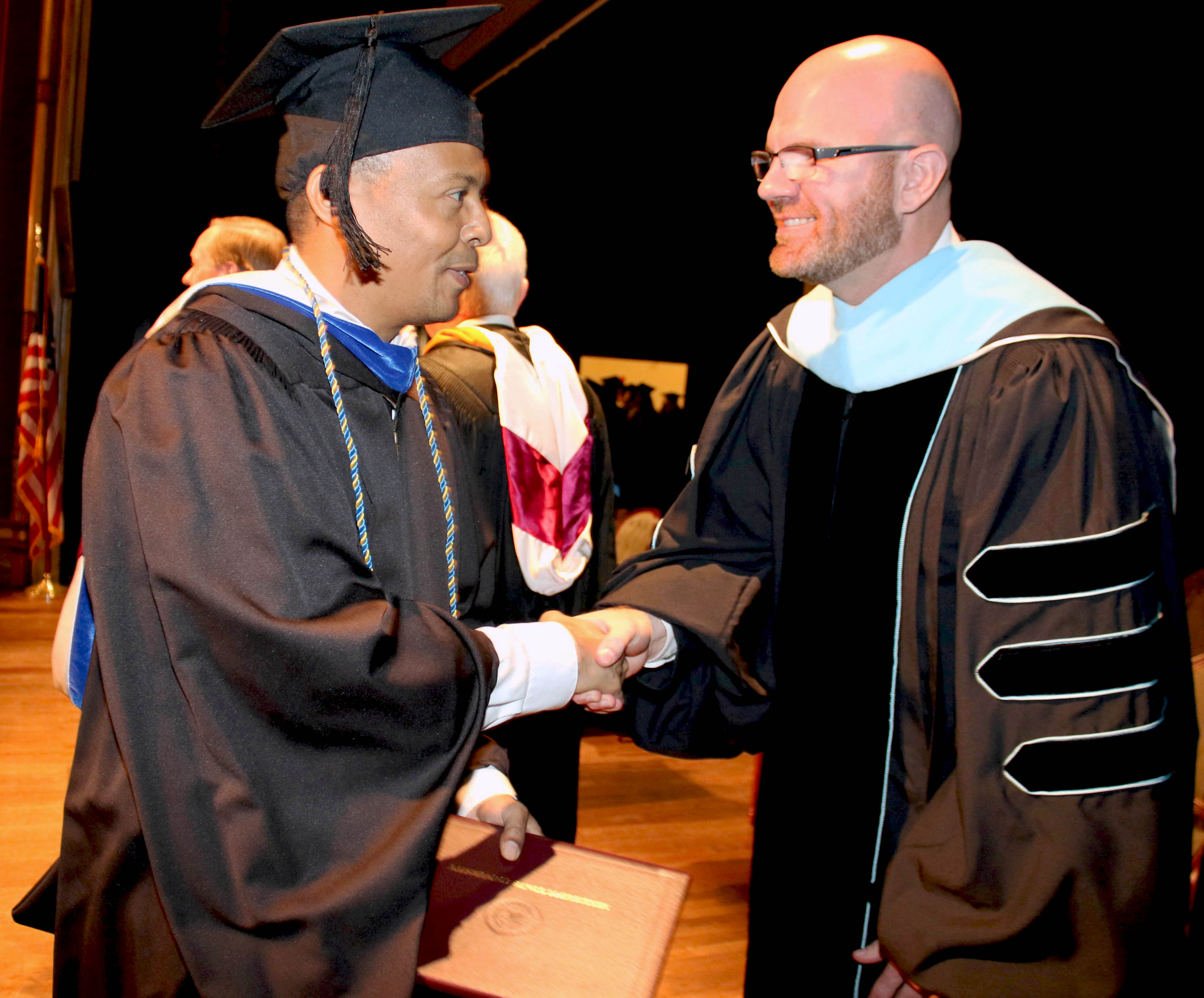 Dr. Cruse shakes hands with recent graduate in cap and gown at commencement ceremonies.  