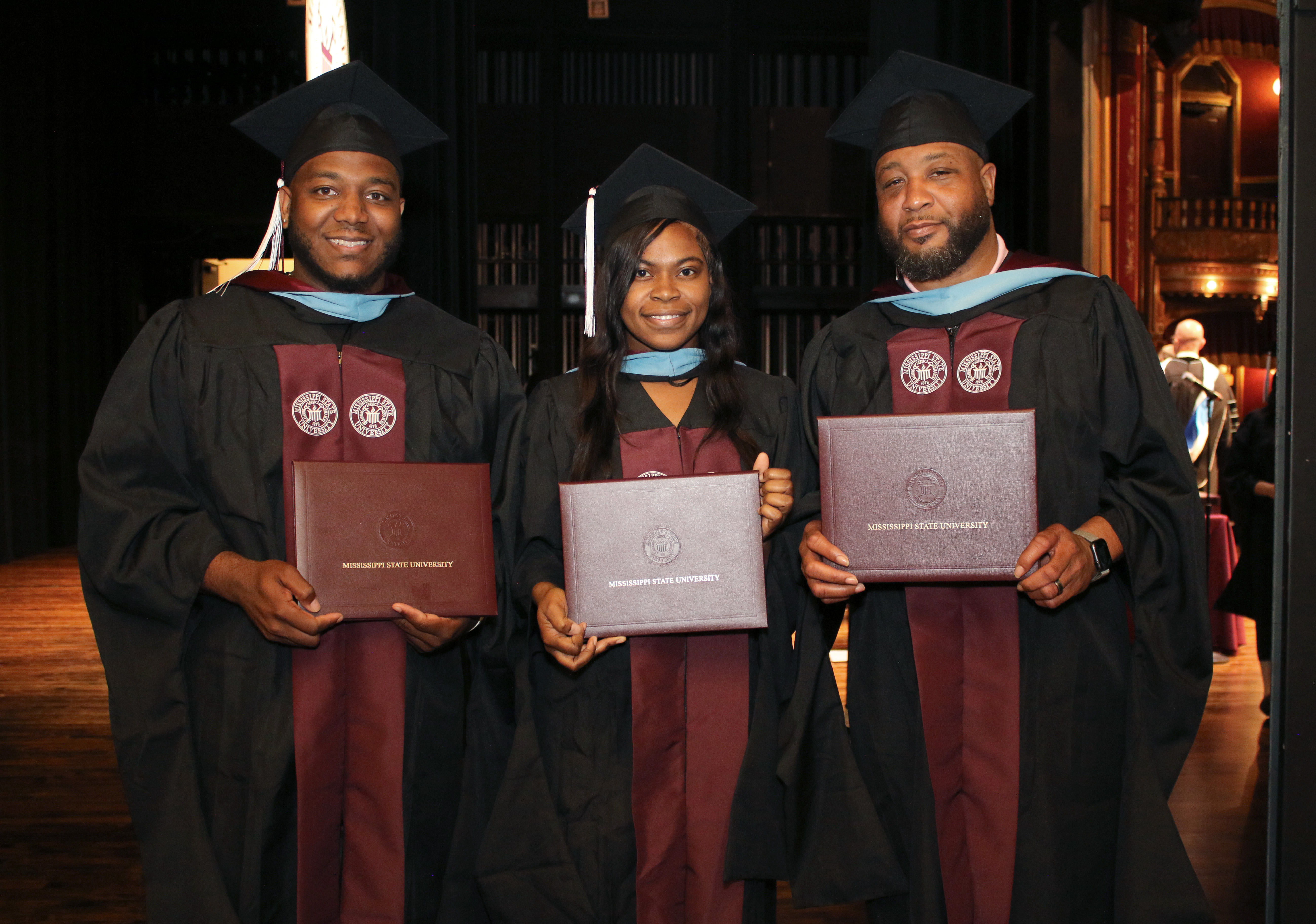 three african american graduates in caps and gowns with diplomas