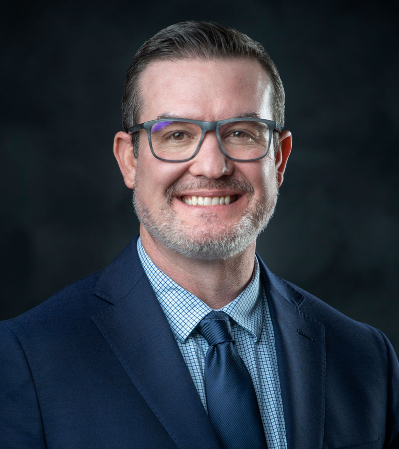 portrait of Jeff Leffler wearing glasses a blue shirt and jacket with a navy tie