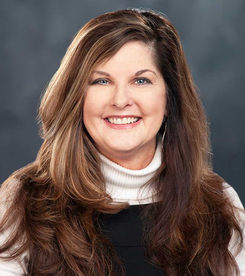 Portrait of Karen Kimberl wearing a white turtle neck with a black vest and full long brown hair