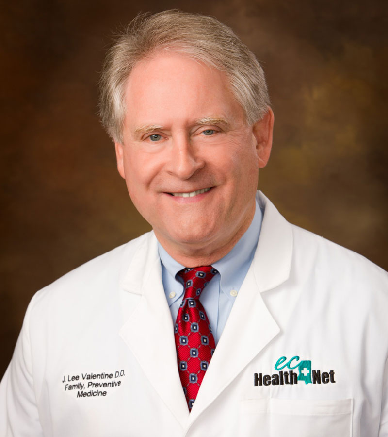 Portrait of Dr. Lee Valentine wearing a white medical coat with a blue shirt and a red tie. 