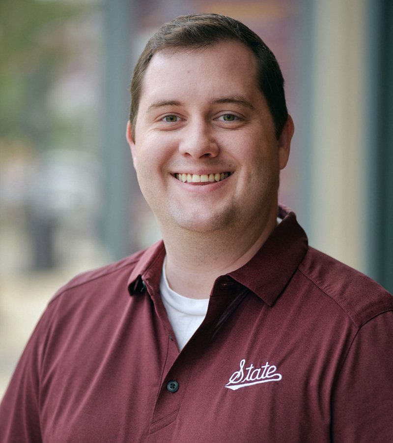 Portrait of Matthew Byrd wearing a maroon polo with the State script logo in white.