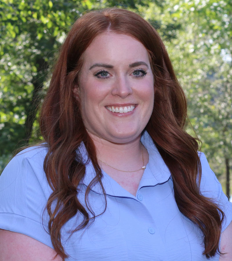 Portrait of Madelyn Baucum wearing a blue shirt and curled long auburn hair. 