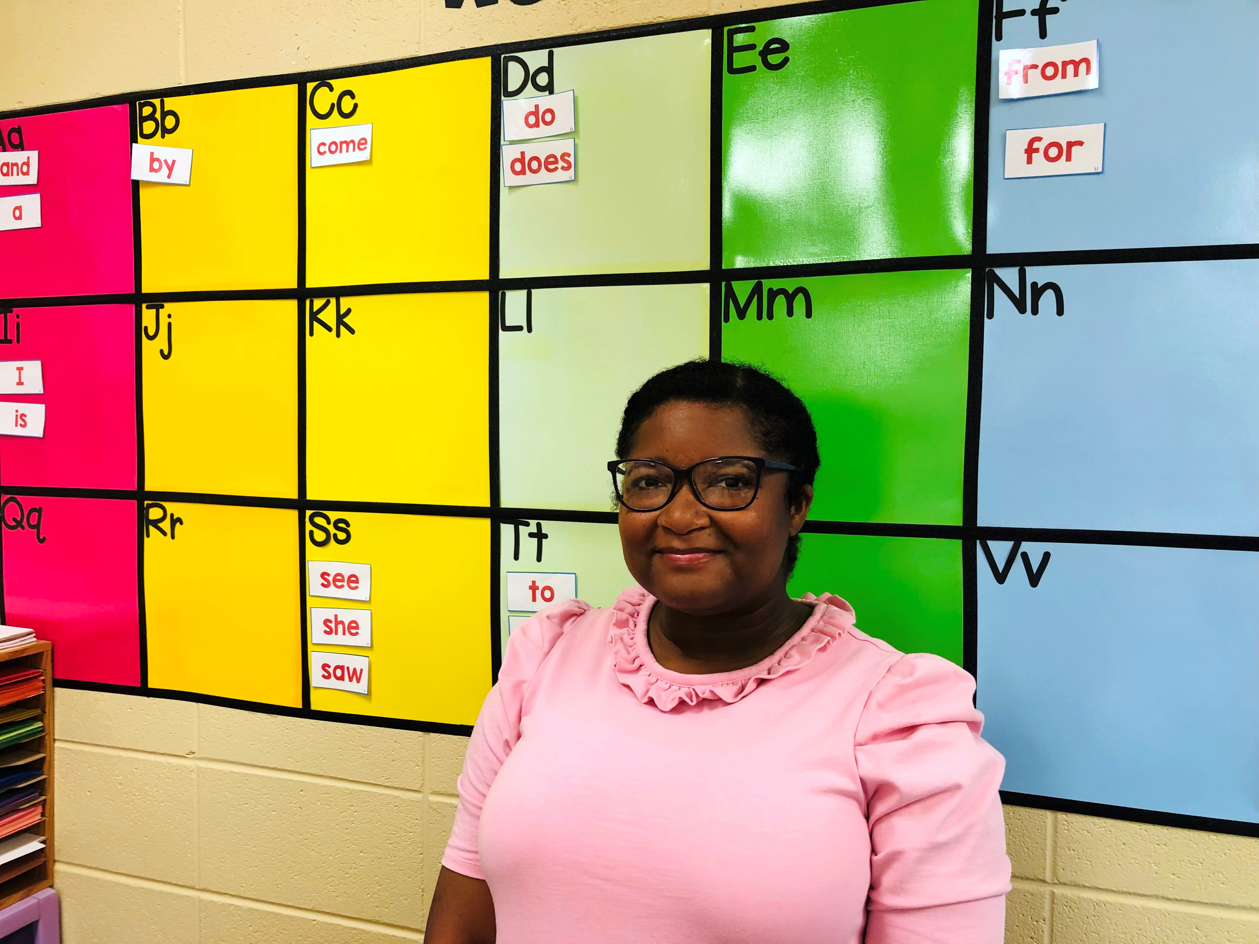 African American woman in pink top in front of bulletin board in classroom