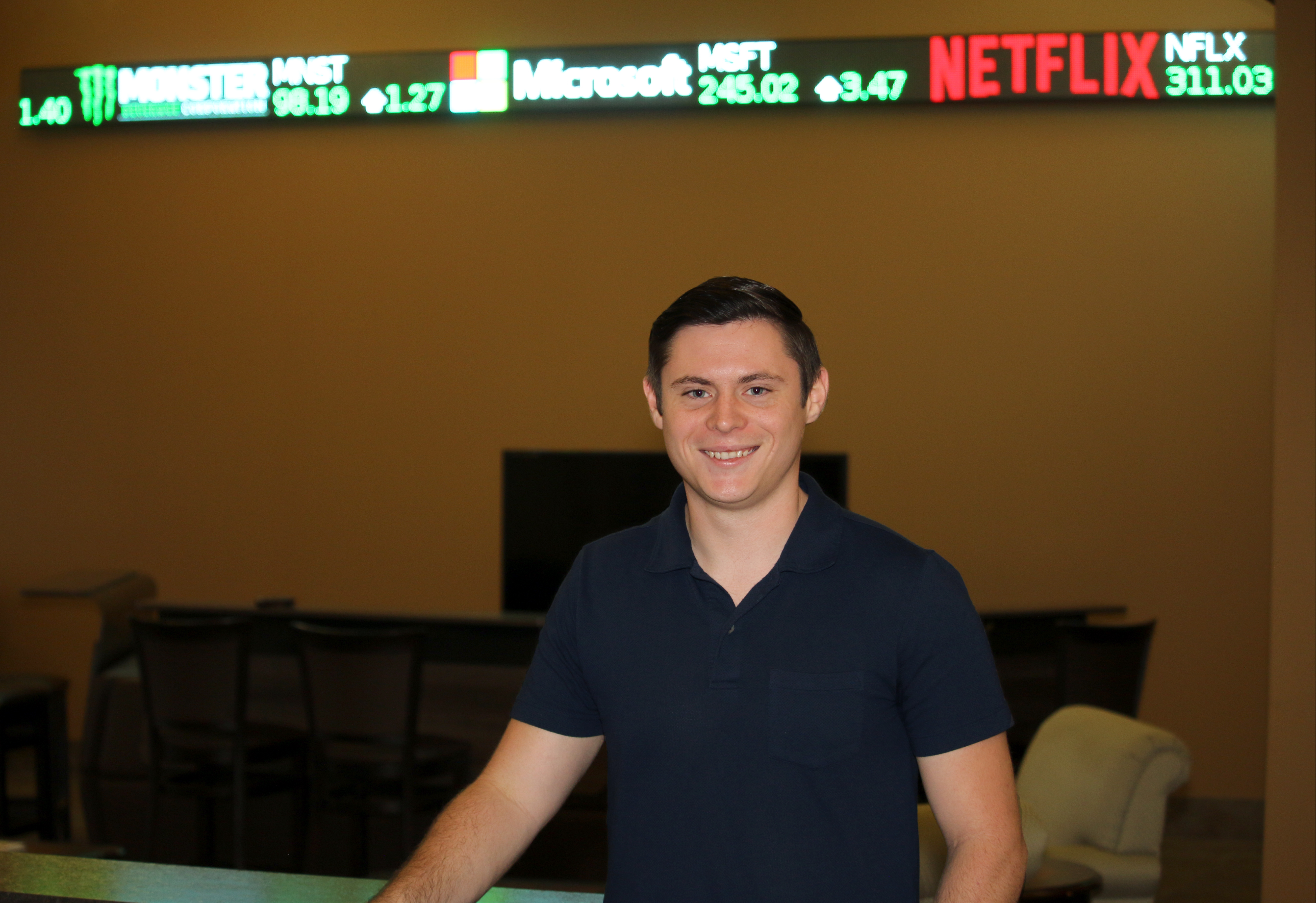 young white male stands in front of a stock ticker