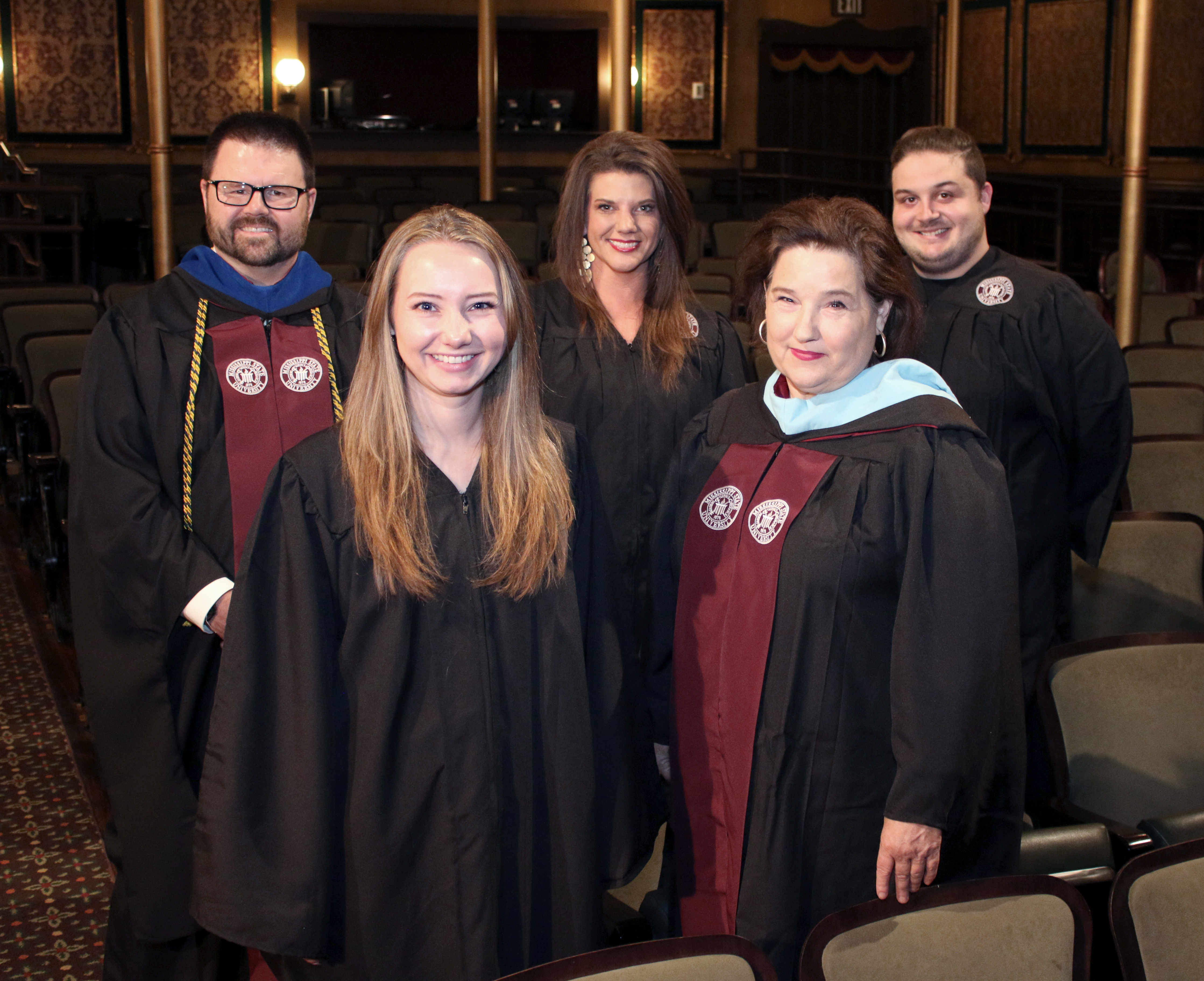 Five outstanding graduates in graduation gowns pose in MSU Riley Center