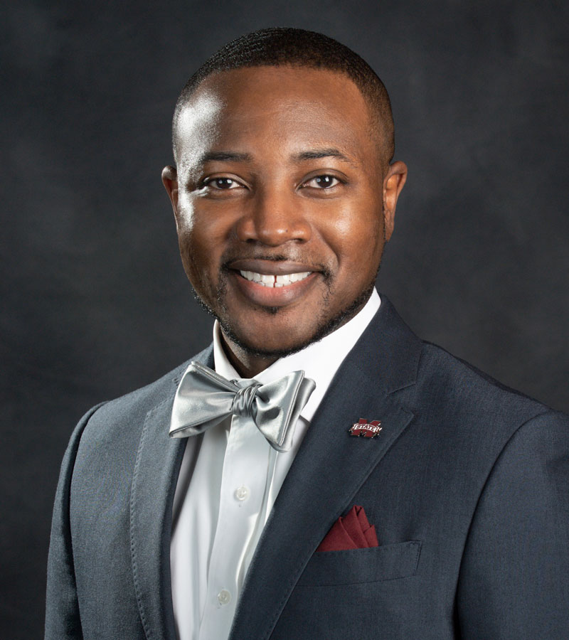 Portrait of Dr. Cedric J. Ruffin wearing navy blazer and blue shirt with silver bow tie and maroon pocket square and lapel pin 