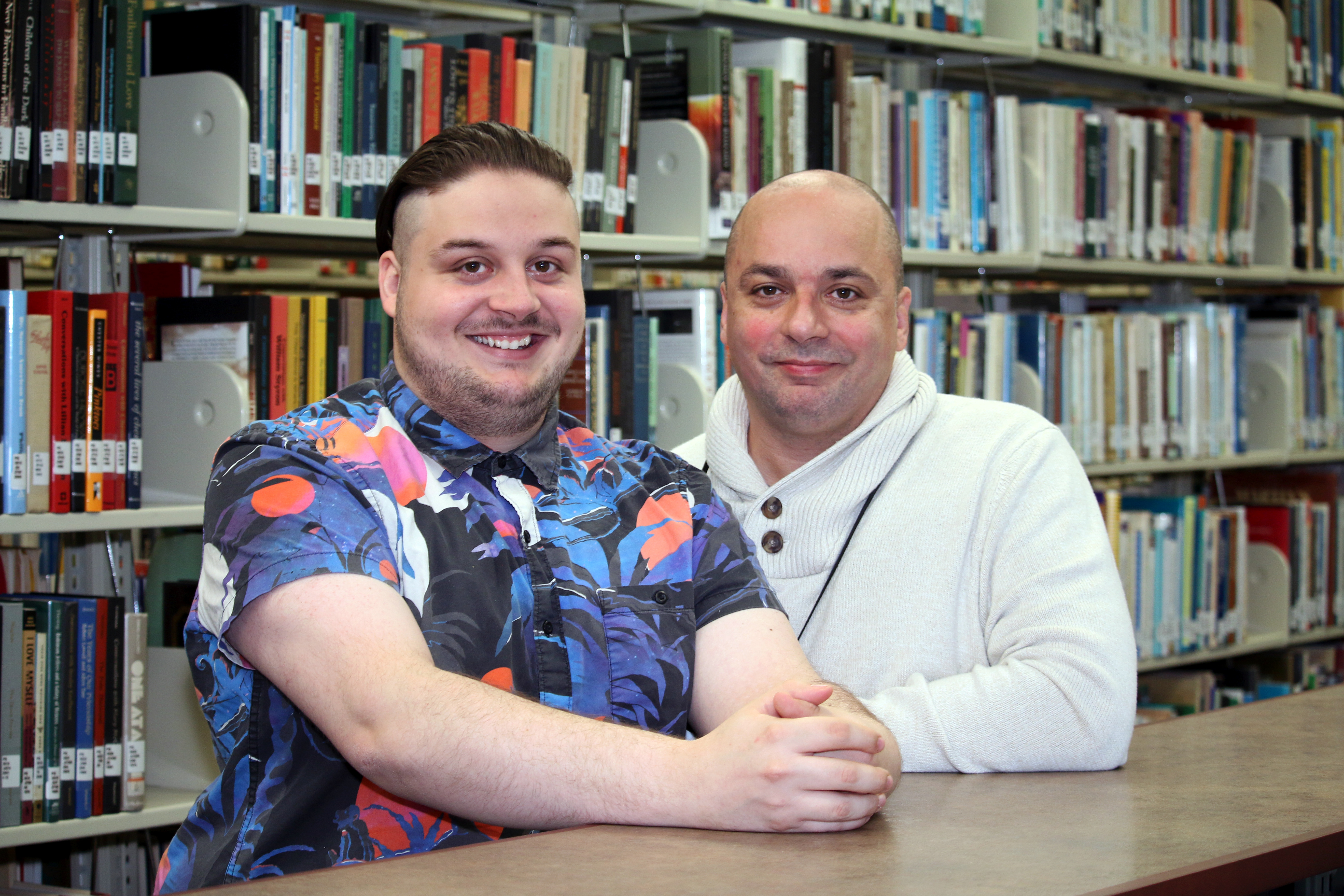 young tall white male and shorter bald male stand in library