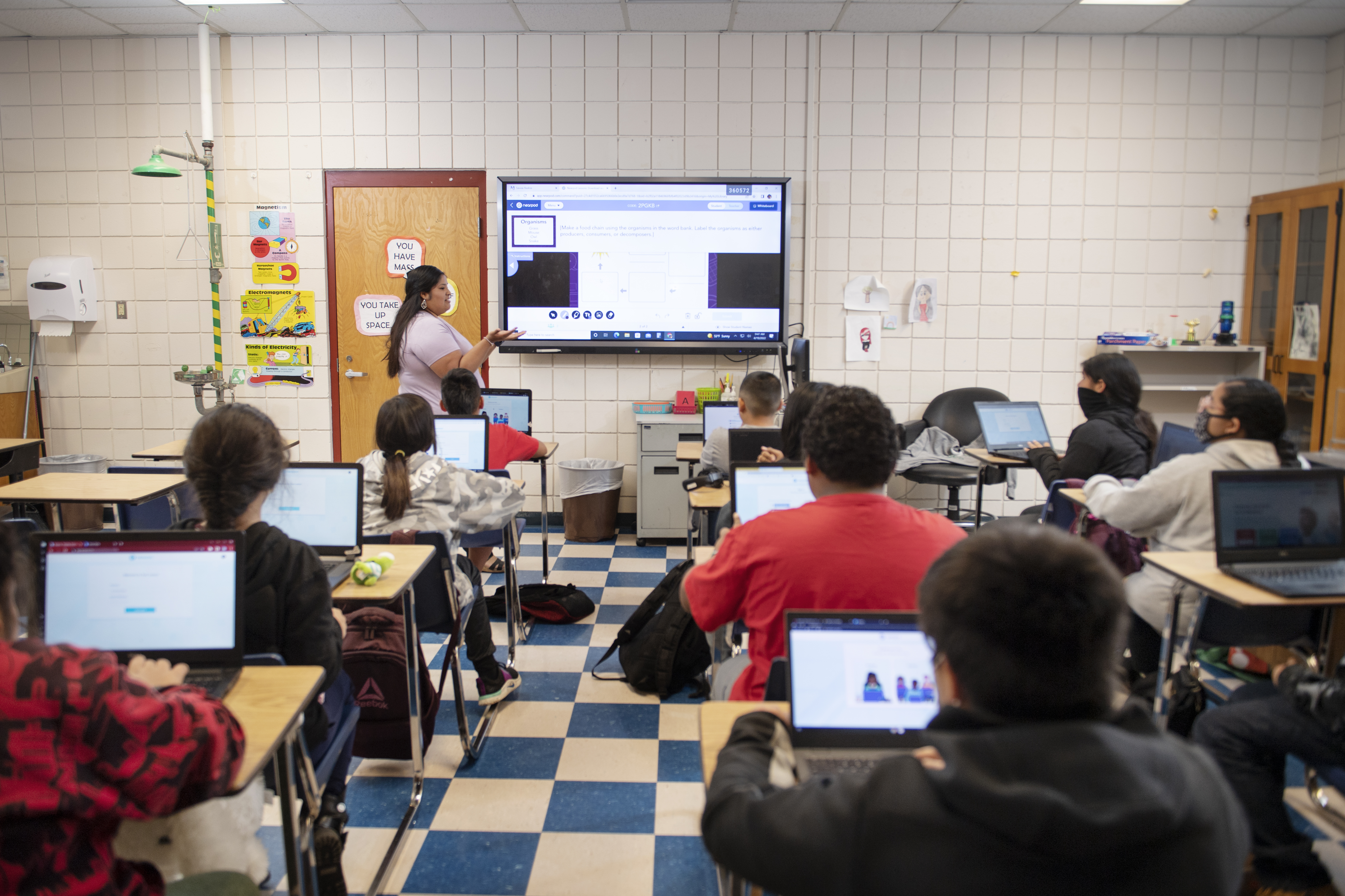 Choctaw young woman with dark hair in classroom with video screen and children