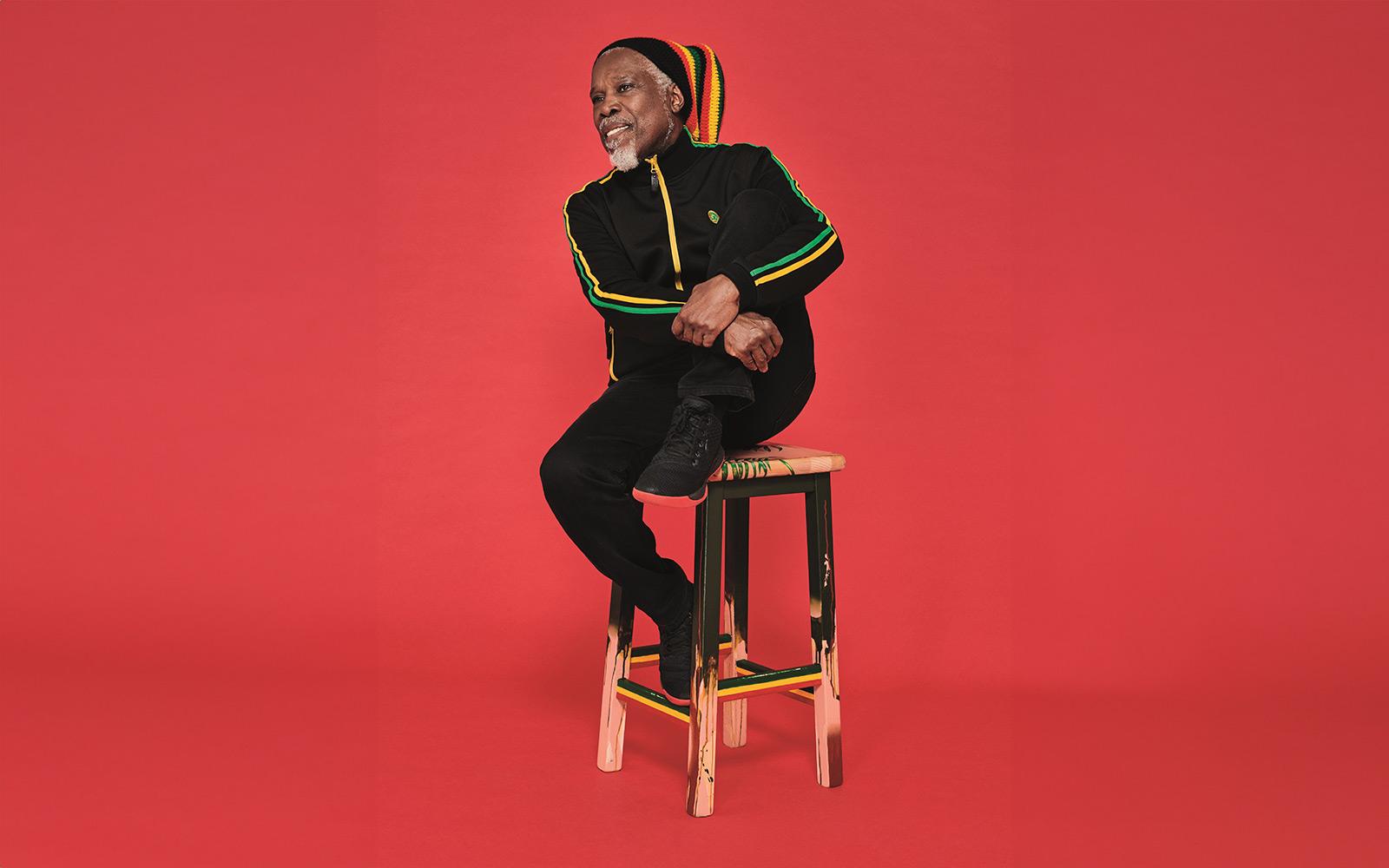 Photo of Billy Ocean sitting on stool in front of red background