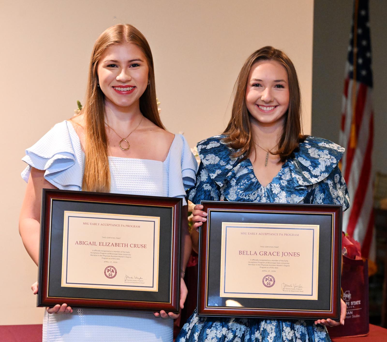 Two students holding framed certificates
