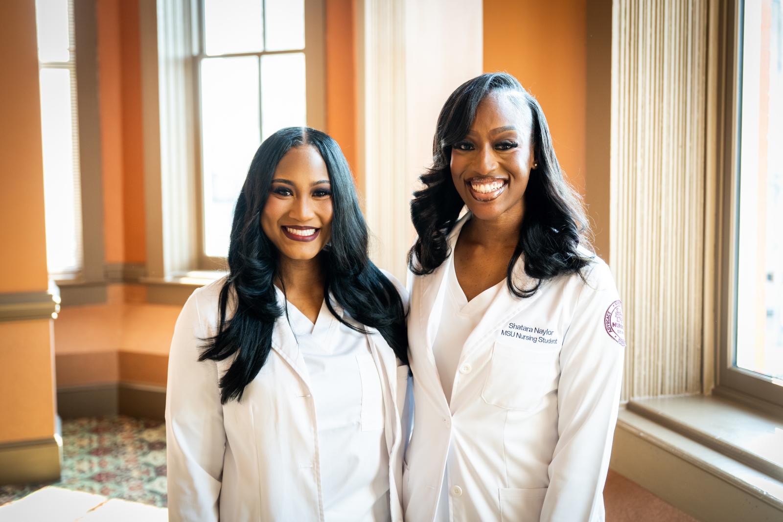 Two MSU-Meridian Nursing graduates in white coats smiling at camera