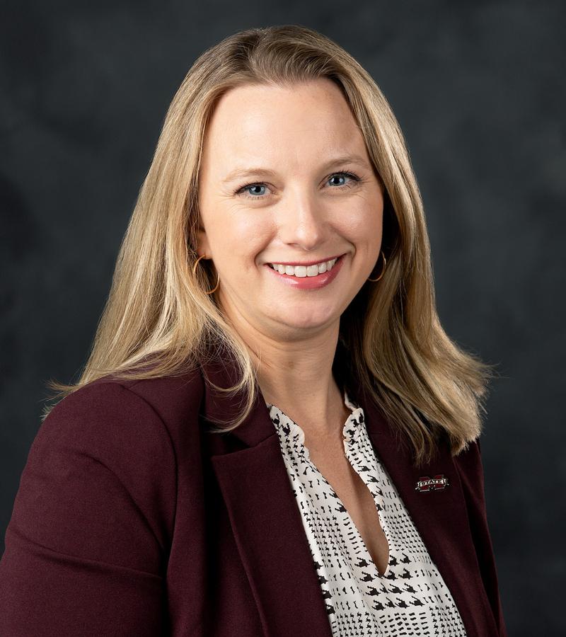 Portrait of Morgan Dudley with light hair wearing a pattern top with a maroon jacket. 